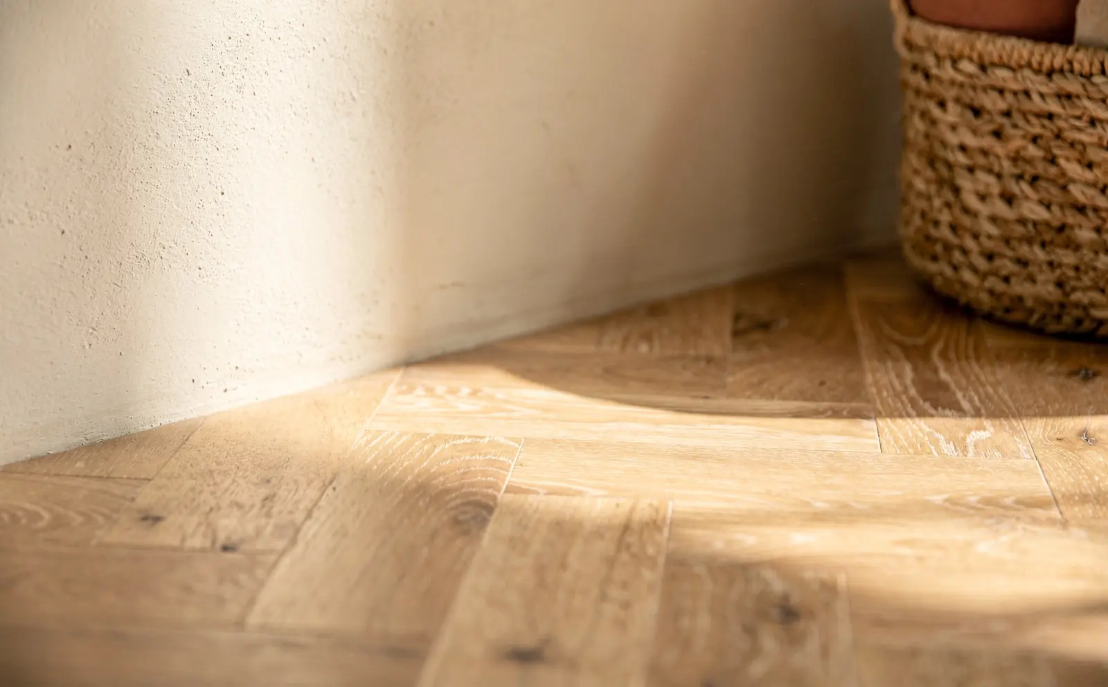 Herringbone oak floor meeting a plaster wall in soft sunlight