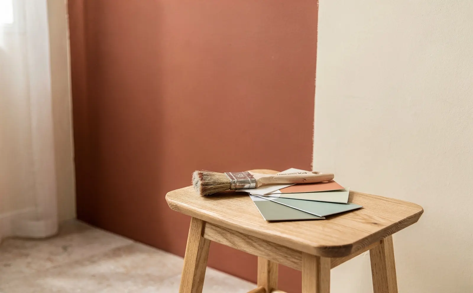 A terracotta painted wall with colour cards on an oak stool
