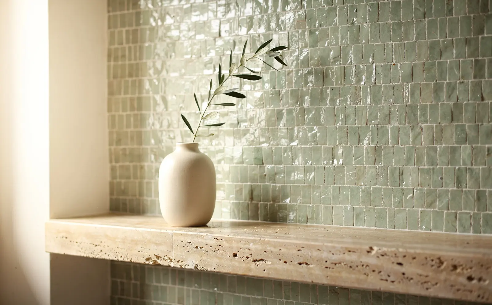 Sage zellige tiles above a travertine ledge with a vase