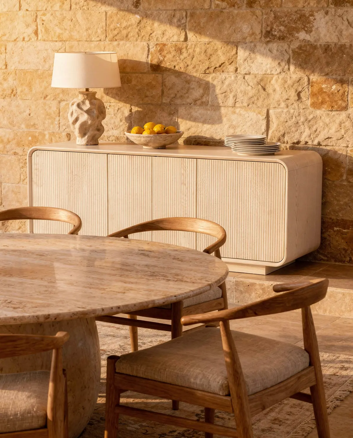 The Alma sideboard behind a round travertine dining table in golden light