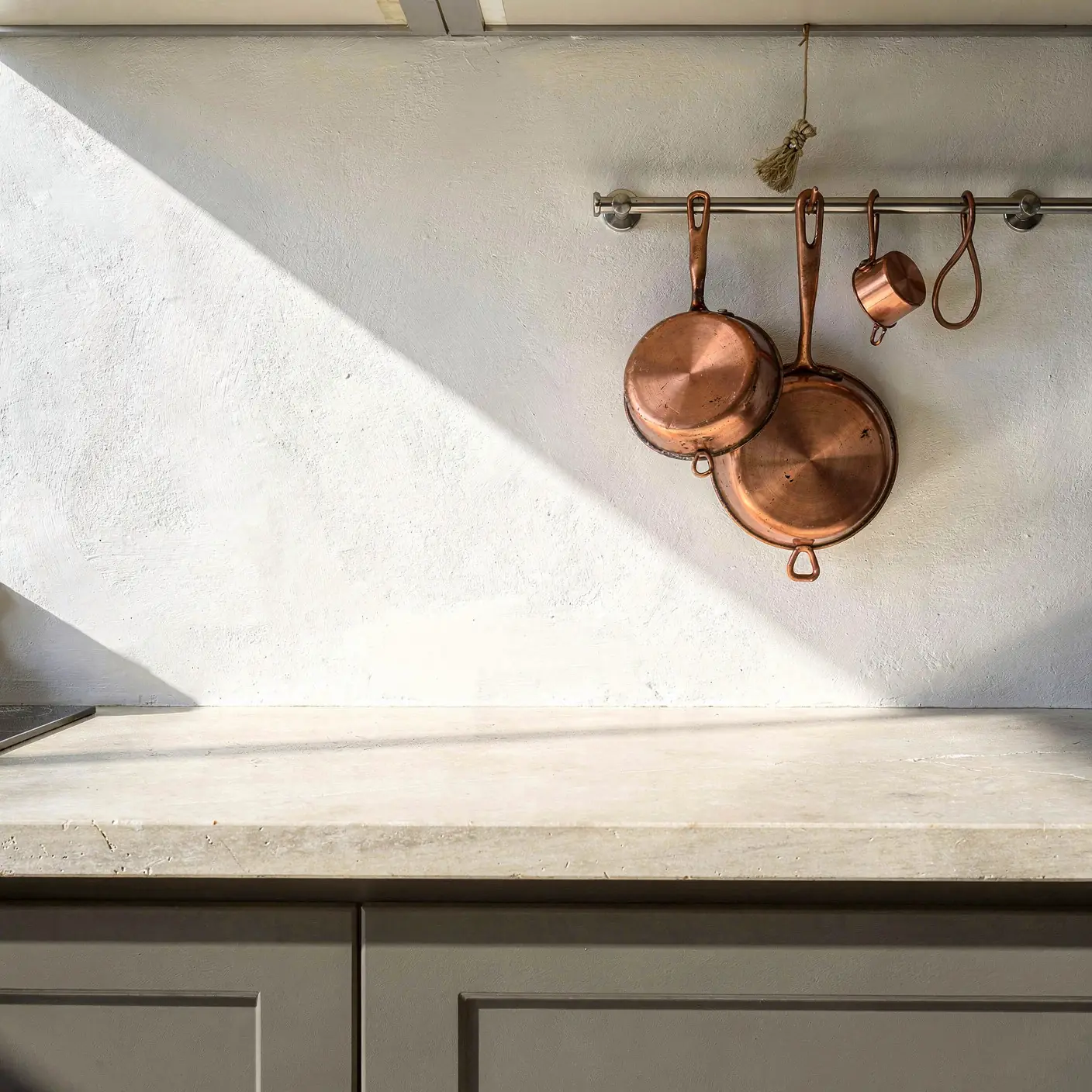 A kitchen backsplash behind a stone worktop with copper pans: Plain wall